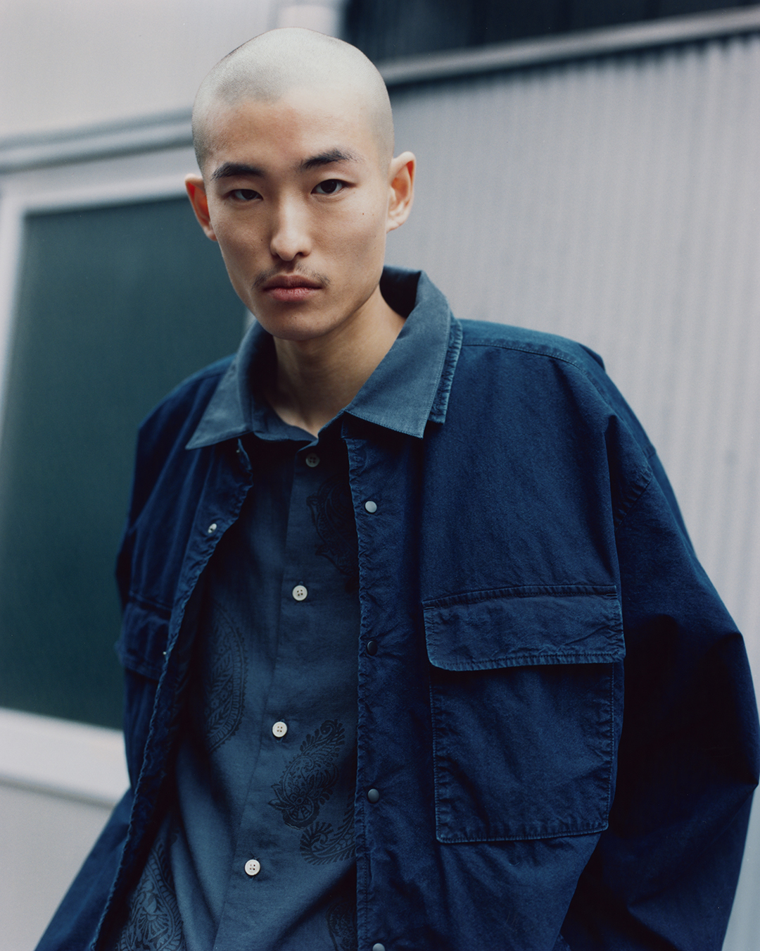 Close-up of a dark blue layered outfit featuring a paisley-patterned shirt and a utility jacket.