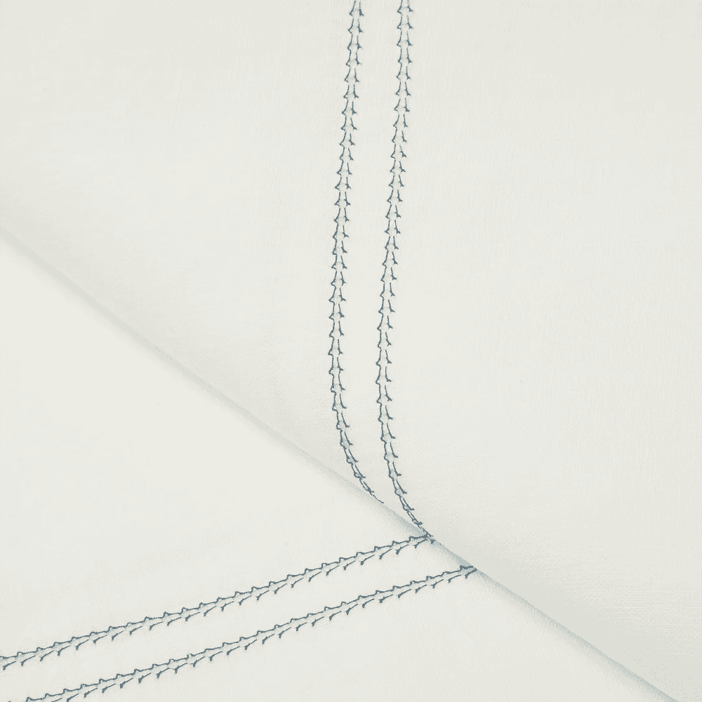 Close-up of white fabric with intricate blue chain-stitch embroidery on the seam.