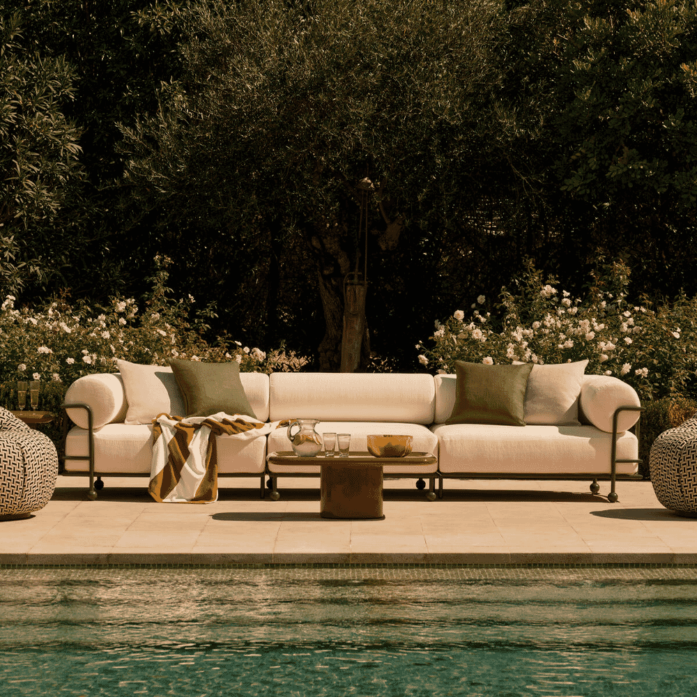 A modern white outdoor sofa with deep green cushions situated next to a swimming pool.