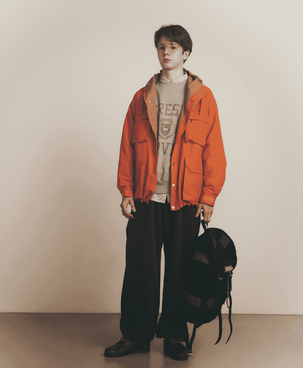 Man modeling a vibrant orange hooded mountain parka with a black backpack.