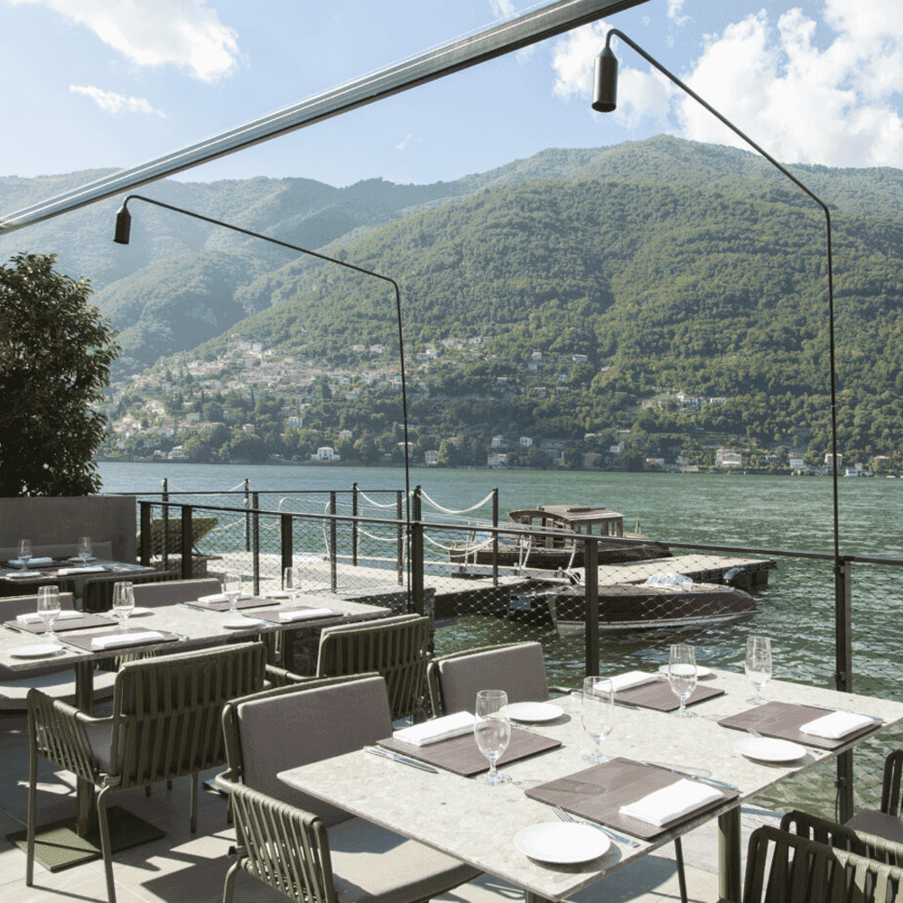 Modern outdoor restaurant terrace overlooking a serene lake and mountain range.