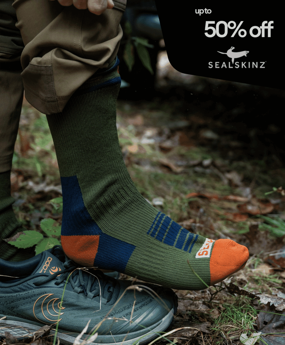 A person in hiking socks and trail shoes standing on a mossy forest floor.