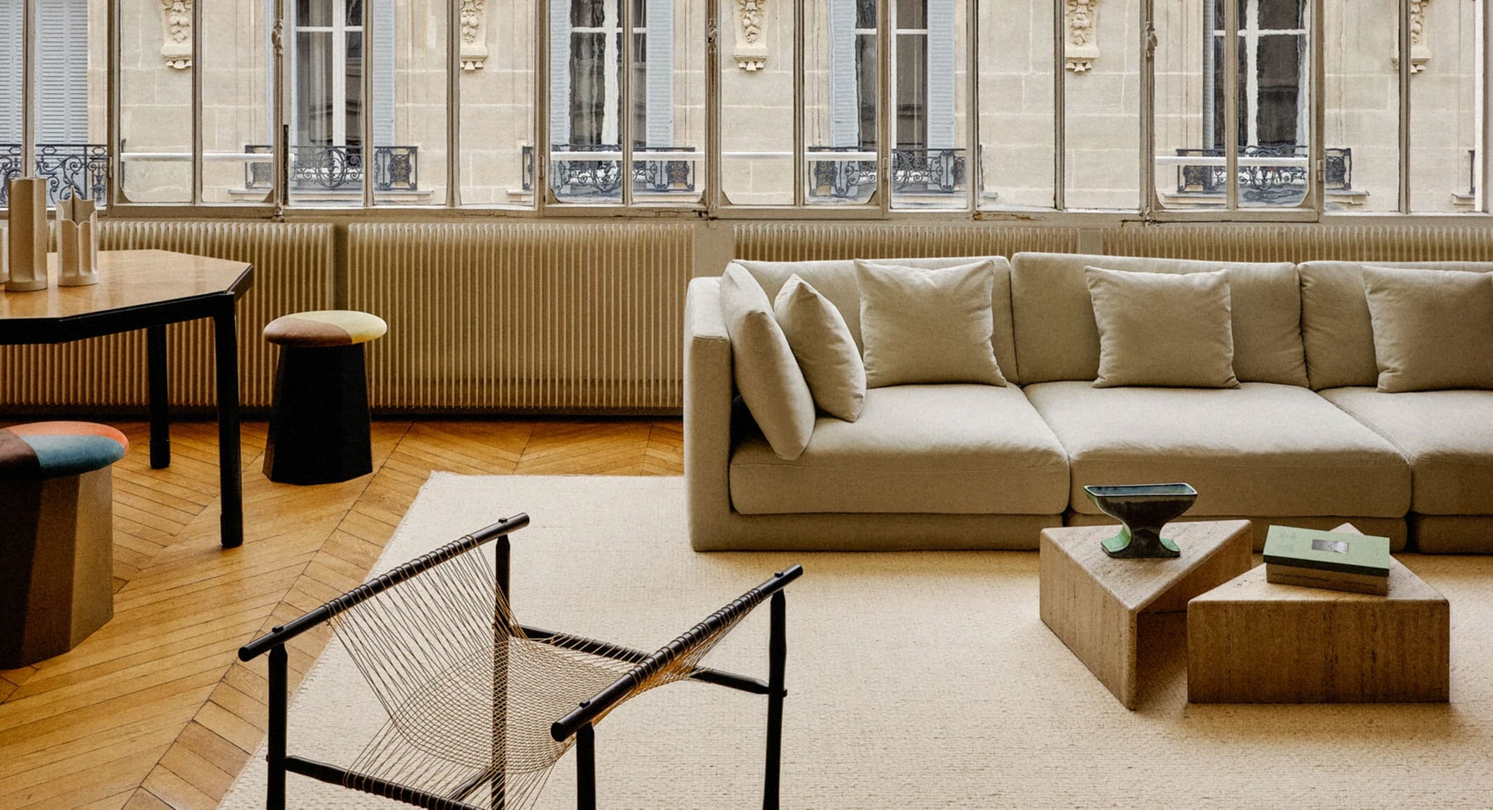 Spacious modern living room with stone coffee tables, a neutral sofa, and views of a European city courtyard.