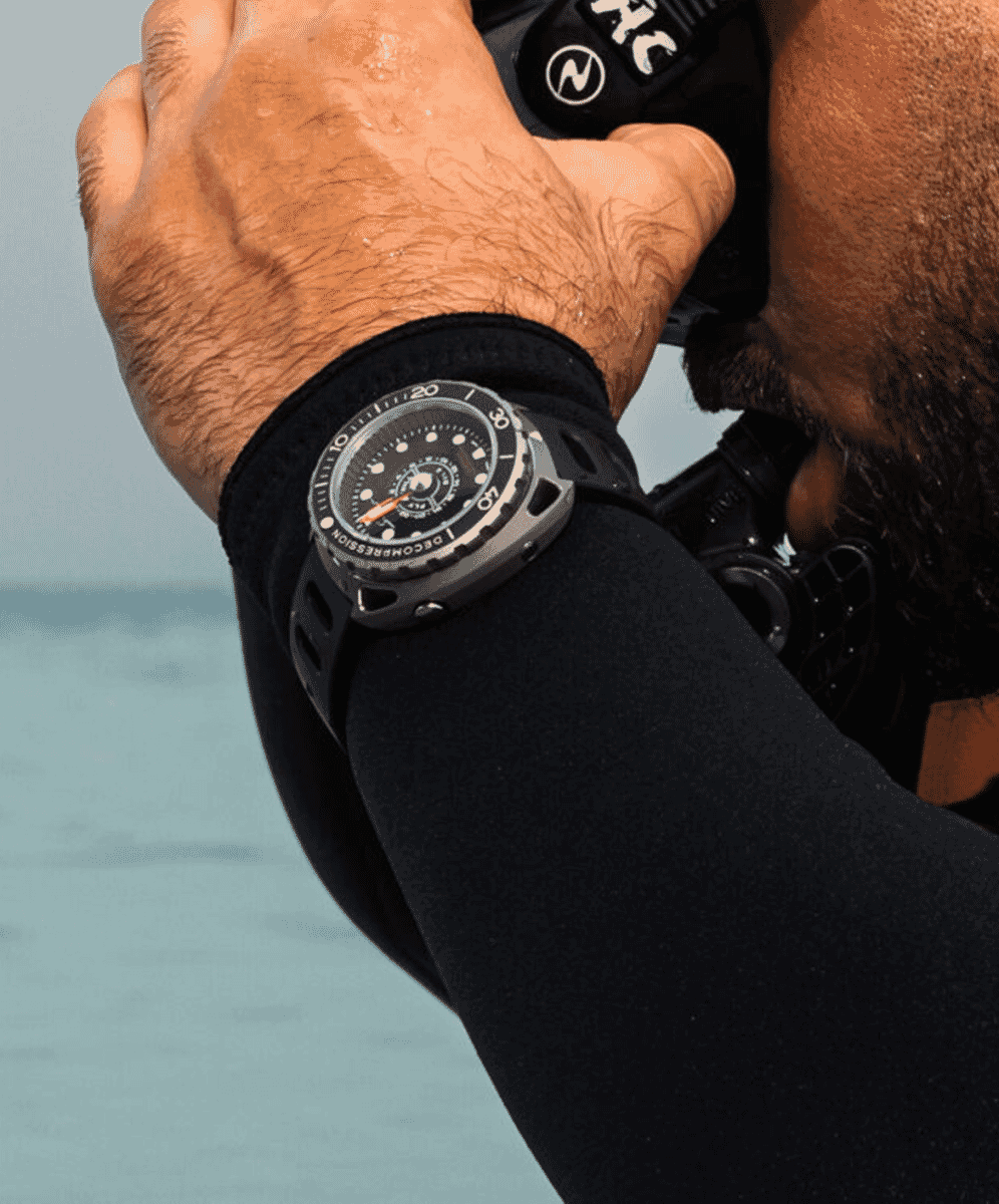 A man in a black wetsuit adjusting his diving gear while wearing a rugged dive watch with an orange hand.