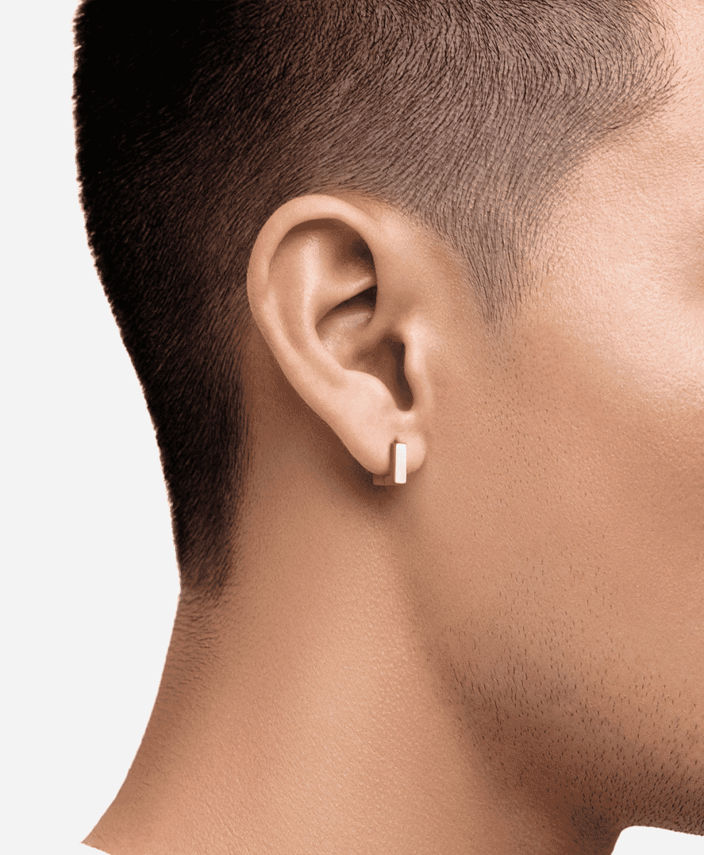Close-up profile of a man wearing a small gold rectangular stud earring.