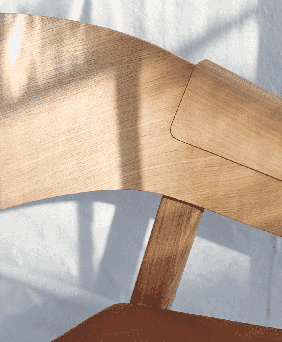 Macro shot of smooth natural oak grain and curved wooden chair frame under soft lighting.