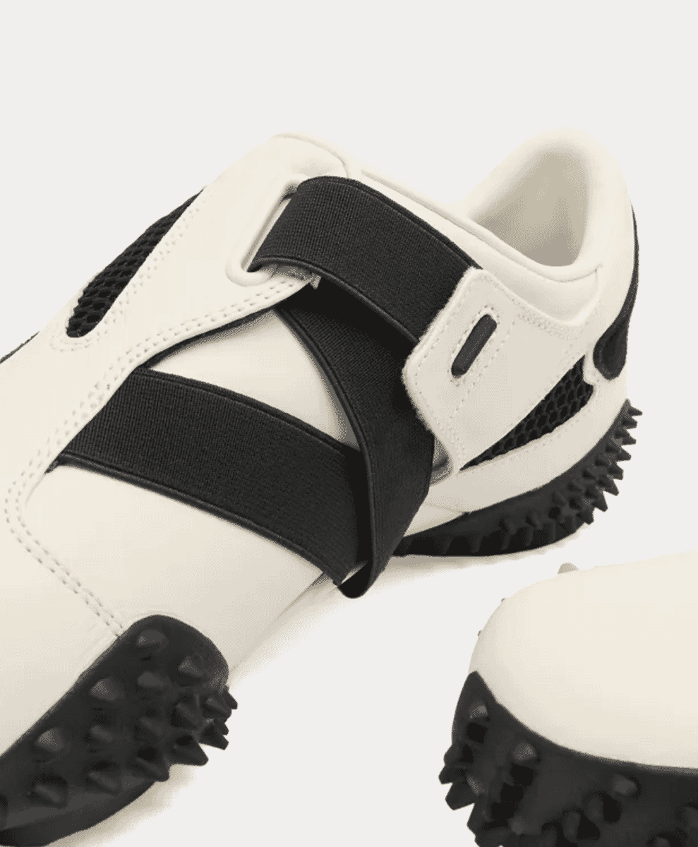 Close-up of a warm white Puma Ur Mostro sneaker with black accents and spike sole.