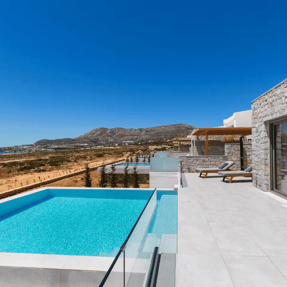 Luxurious modern villa with stone architecture and an infinity pool overlooking a coastal landscape.
