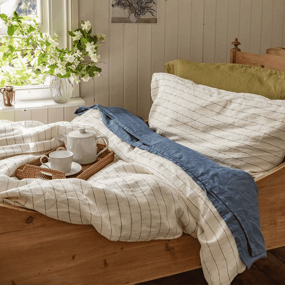 A wooden bed with striped linen bedding, a blue throw, and a tea tray.