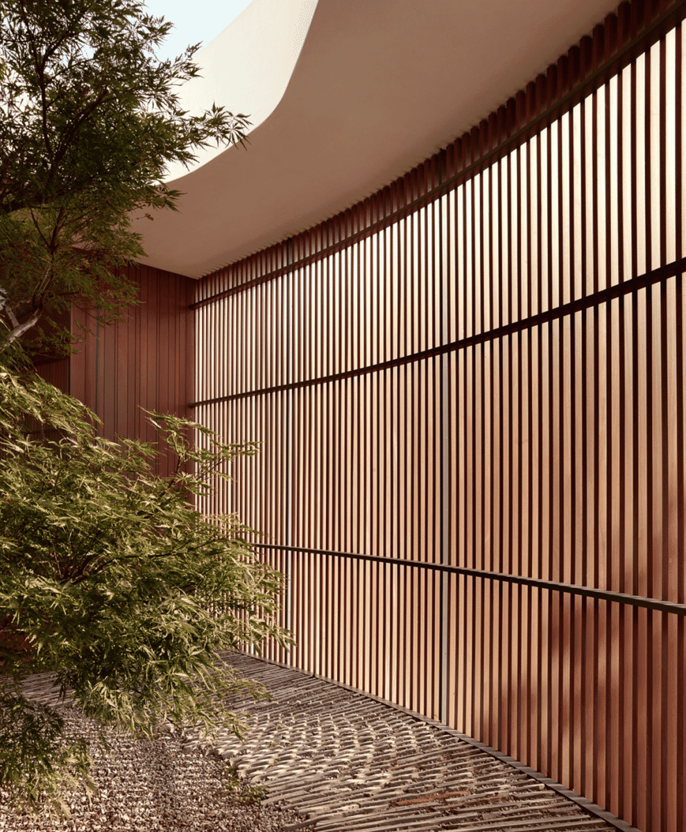 Close-up of a curved wooden slat wall and a gravel garden path.