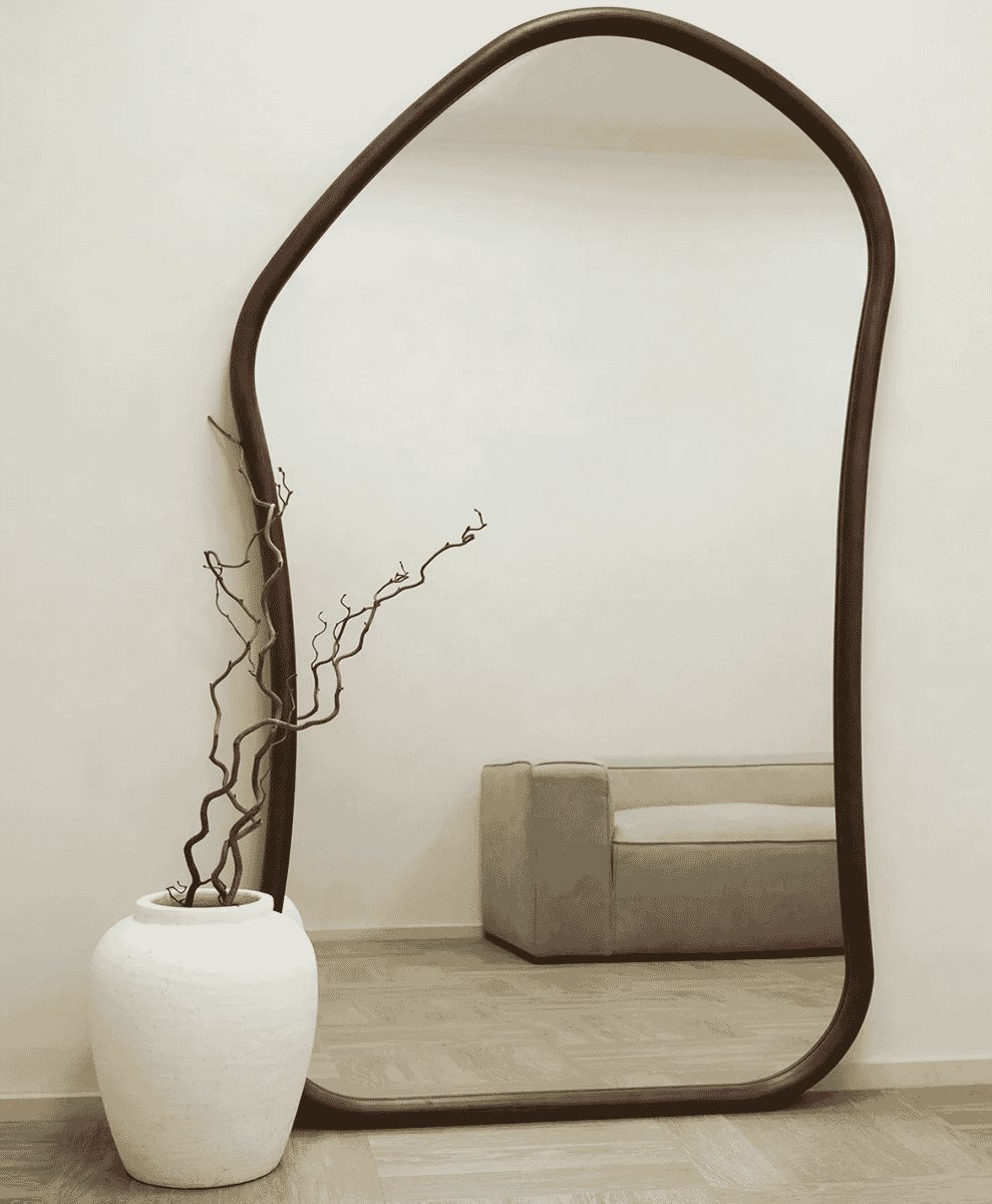 Large organically shaped dark wood mirror beside a white vase with decorative branches.