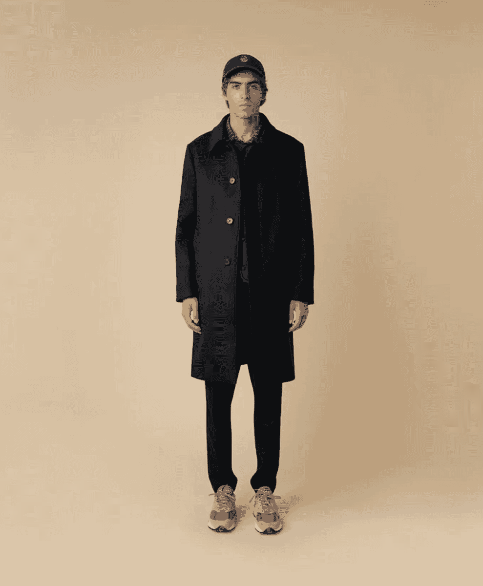 A man in a black wool coat with wooden buttons and a baseball cap.