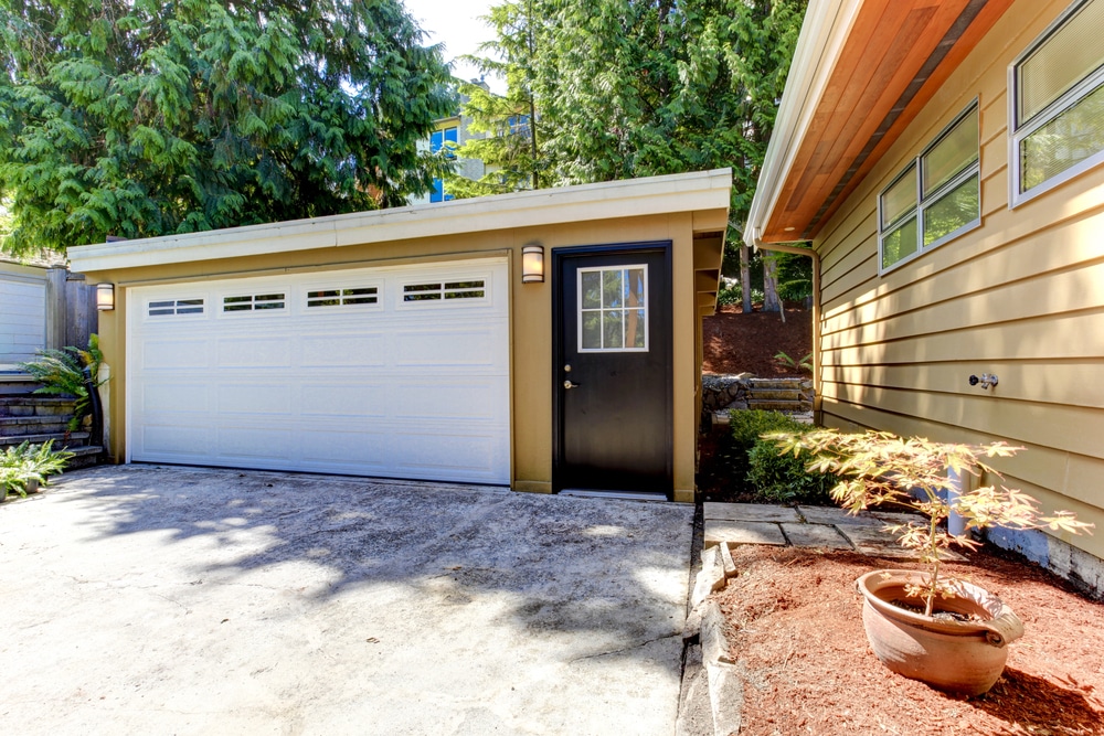 Side view of a garage showing its proximity to the main house with yellow siding and garden beds.