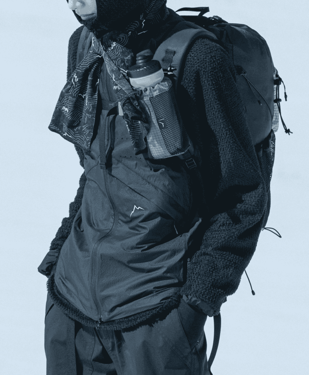 A person wearing a fleece jacket and insulated vest with a hydration backpack