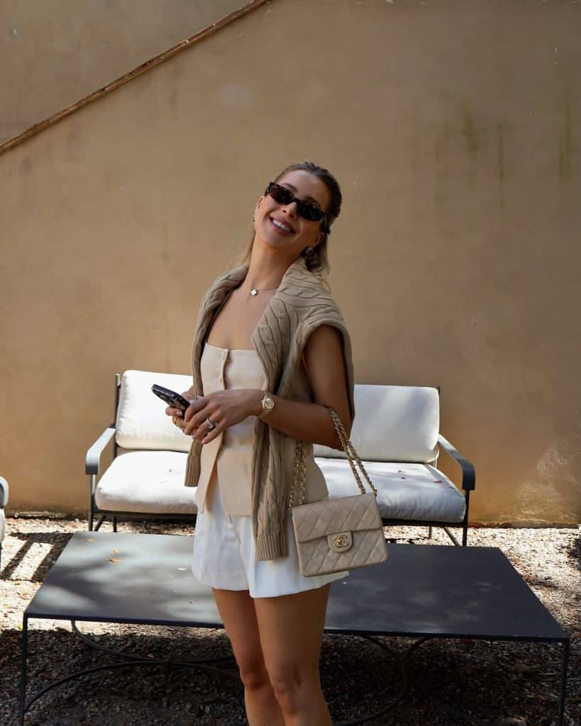 Beige knit vest and white shorts paired with a quilted luxury handbag.