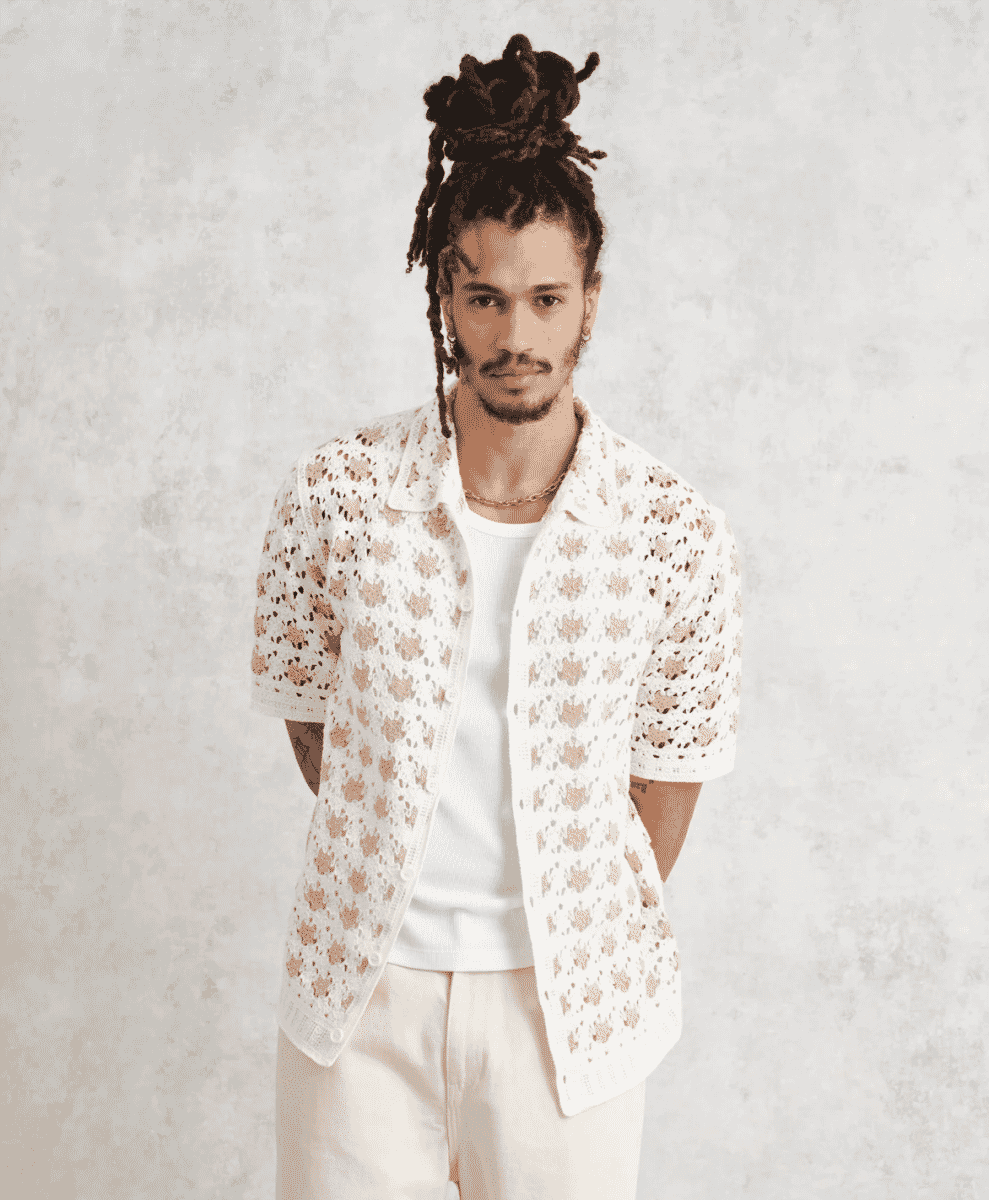A man wearing a white floral lace knitted cardigan over a white t-shirt.
