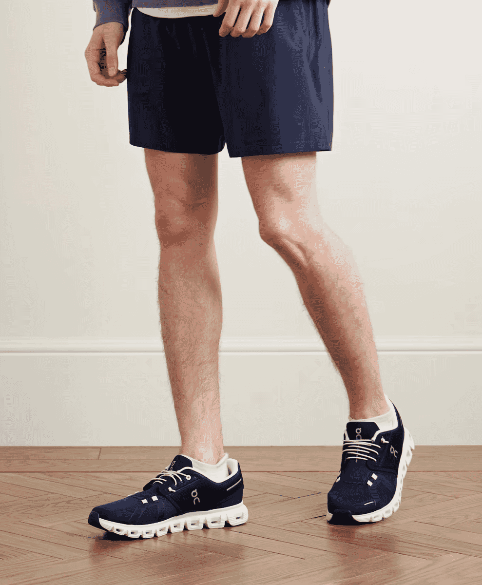 Man wearing navy blue On running sneakers with white soles in a minimalist setting.