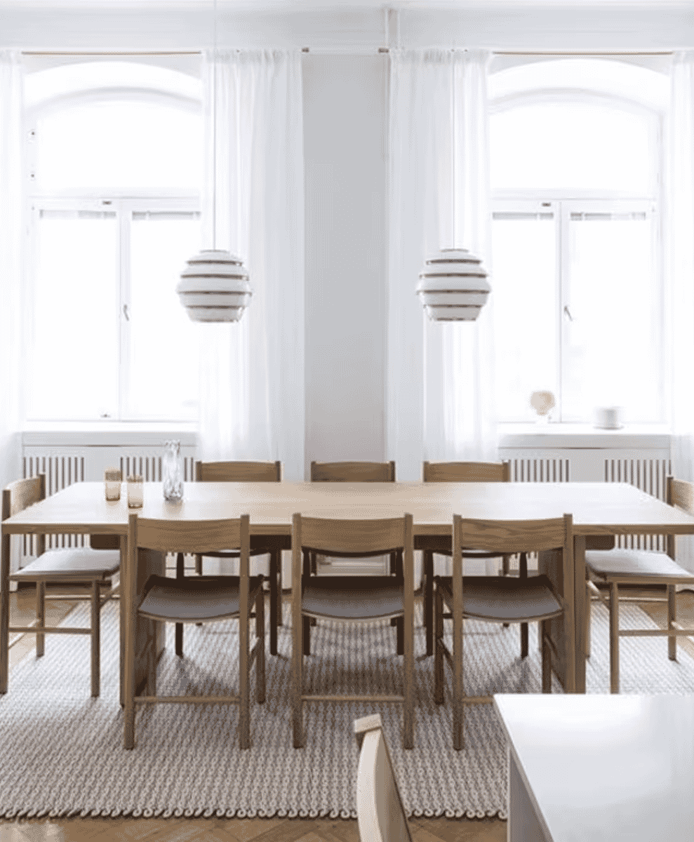 Bright Scandinavian dining room with arched windows, light wood furniture, and minimalist decor.