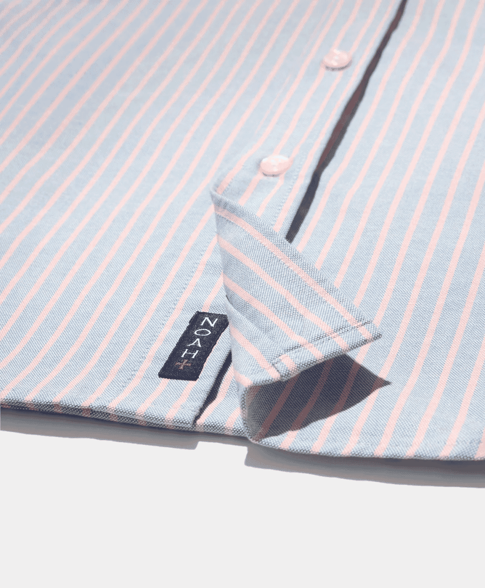 Close-up of a light blue and pink striped button-up shirt with a visible NOAH+ brand tag.