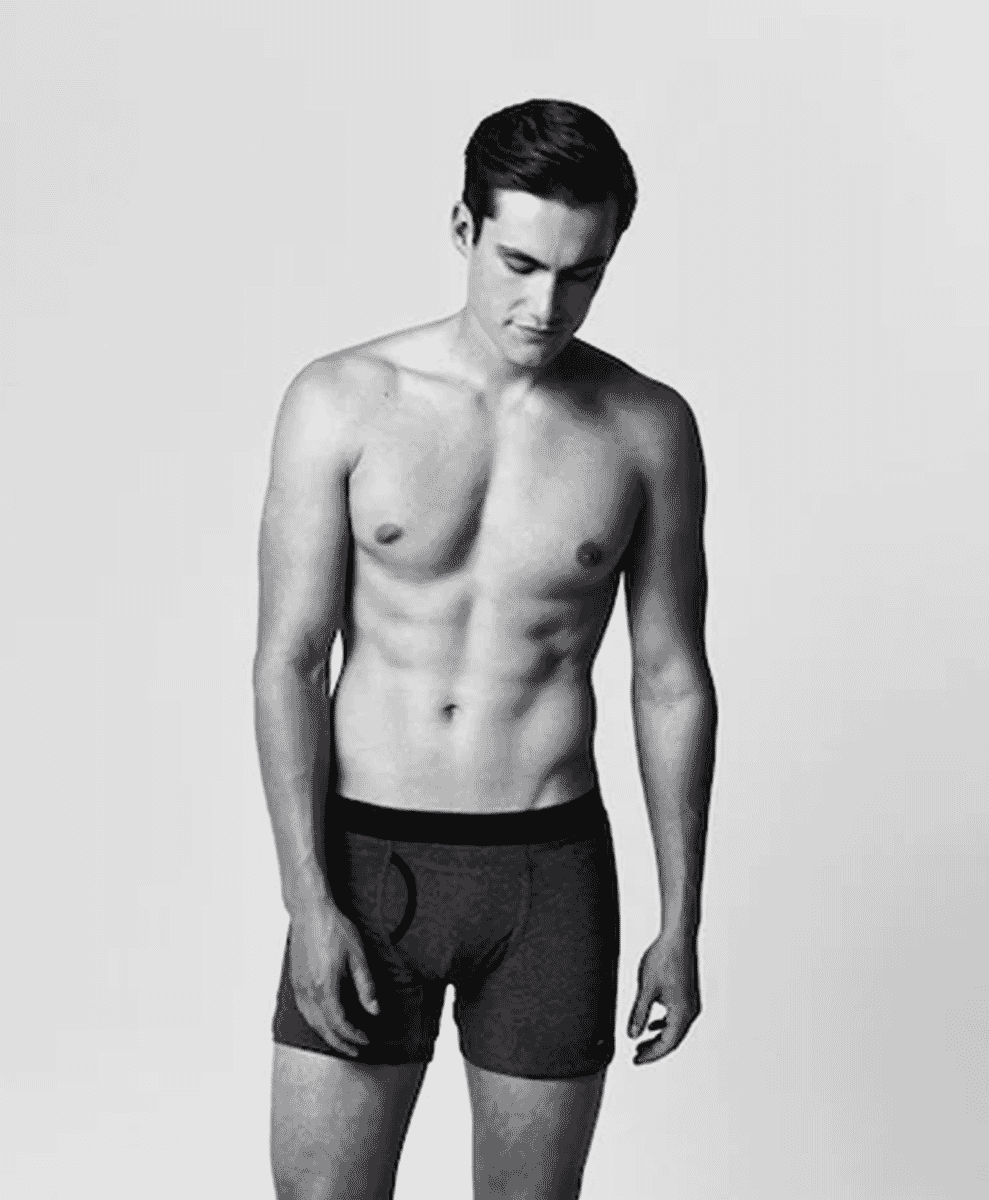 Black and white studio photograph of a muscular man modeling black boxer briefs with a minimalist fit.