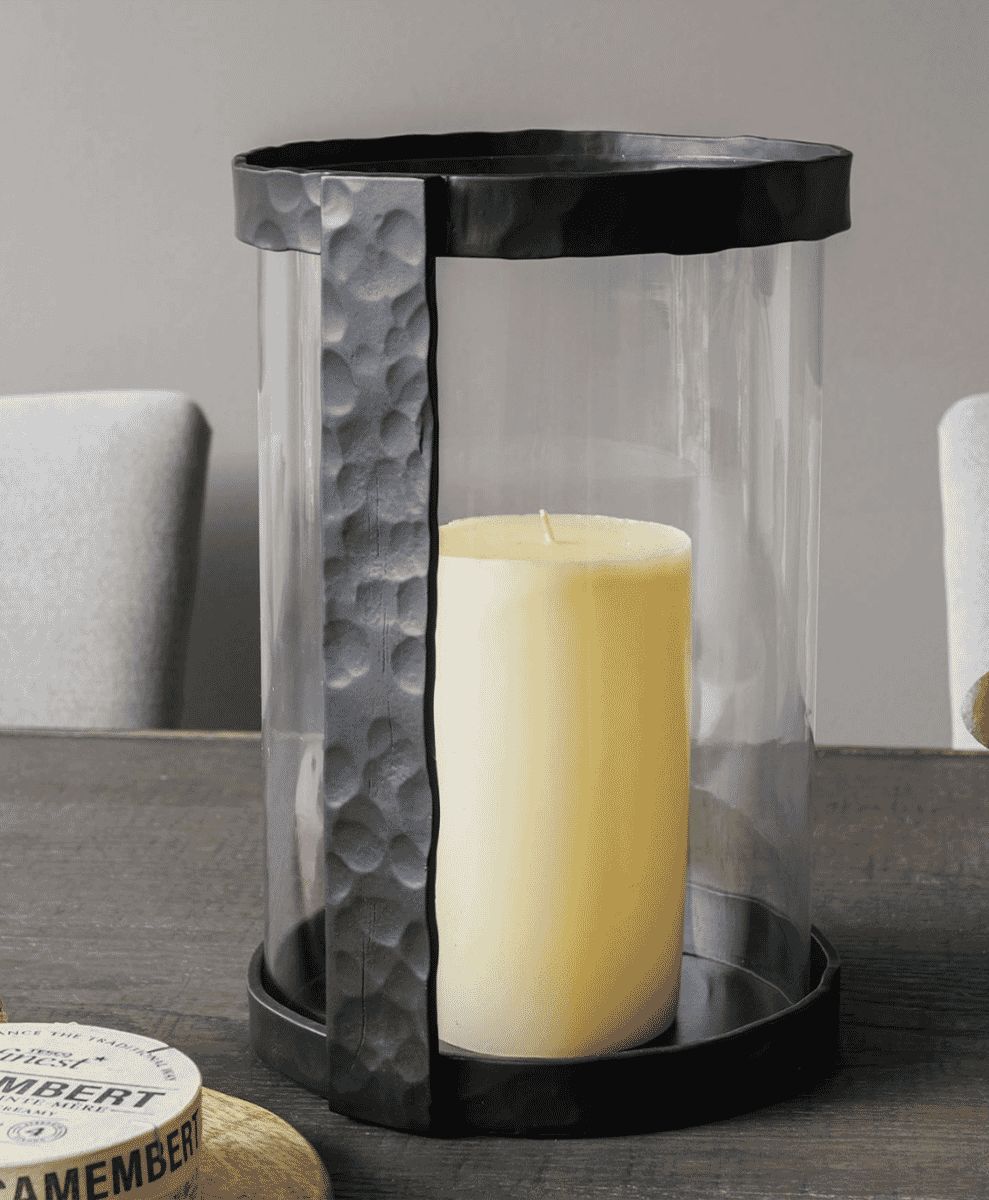 A decorative glass candle lantern with a hammered metal frame on a wooden table.