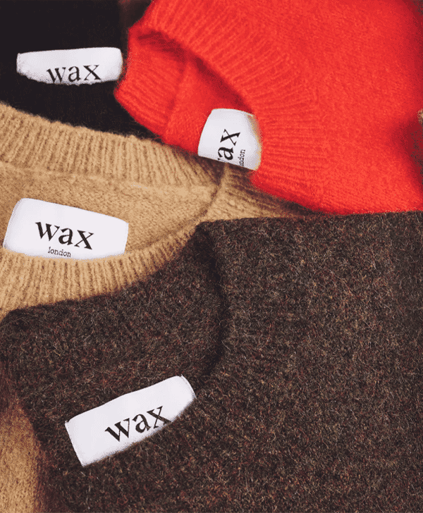 Close-up of four cozy knit sweaters in different colors with Wax London brand labels.
