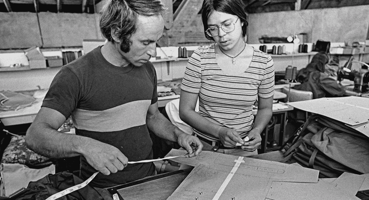 Two people working with fabric patterns and tools in a sewing workshop.