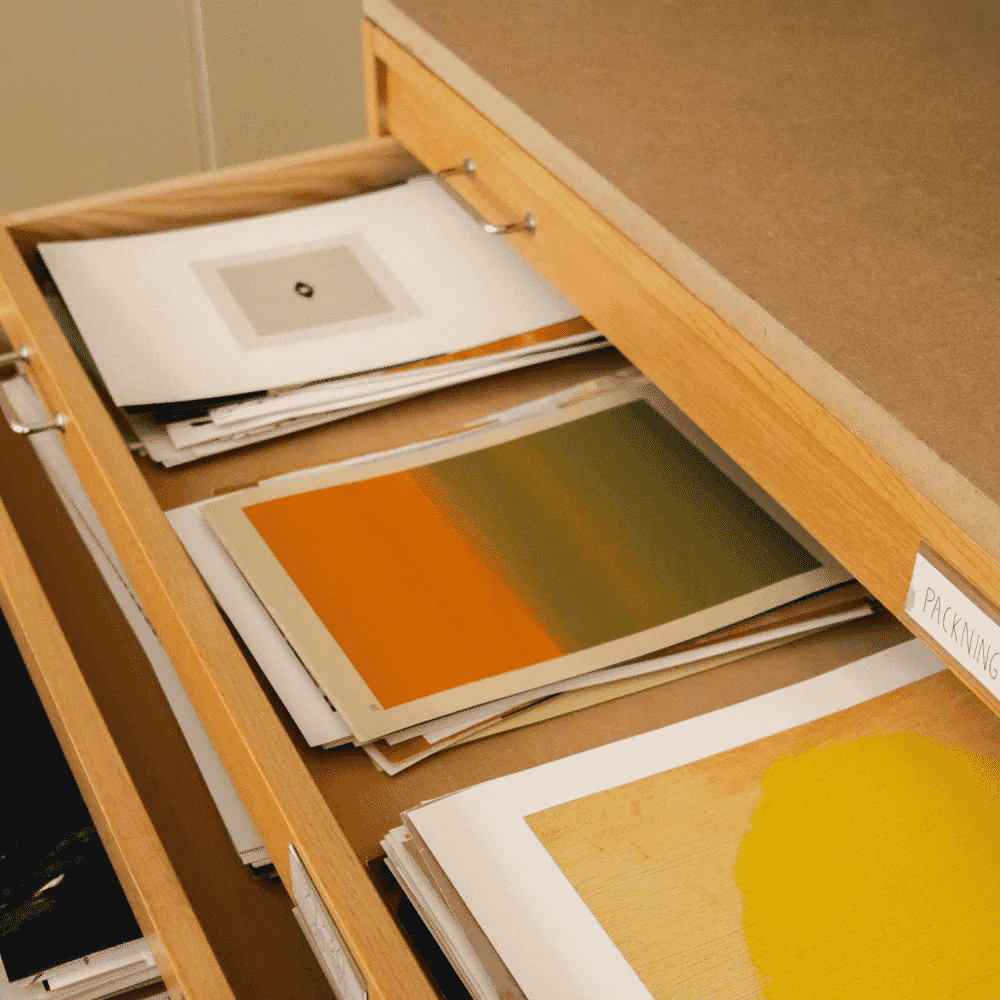 A close-up of a wooden drawer containing art prints and color swatches in terracotta, green, and yellow tones.