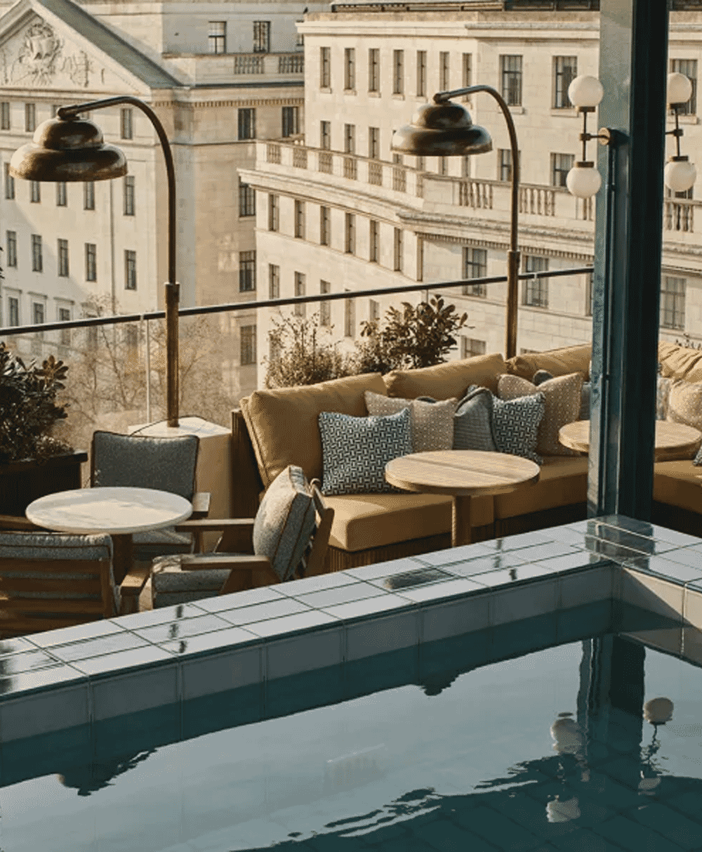 Rooftop lounge with plush seating and a tiled pool overlooking urban architecture.