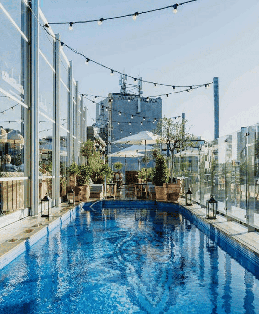 A serene rooftop pool area with string lights and glass railings overlooking the city.