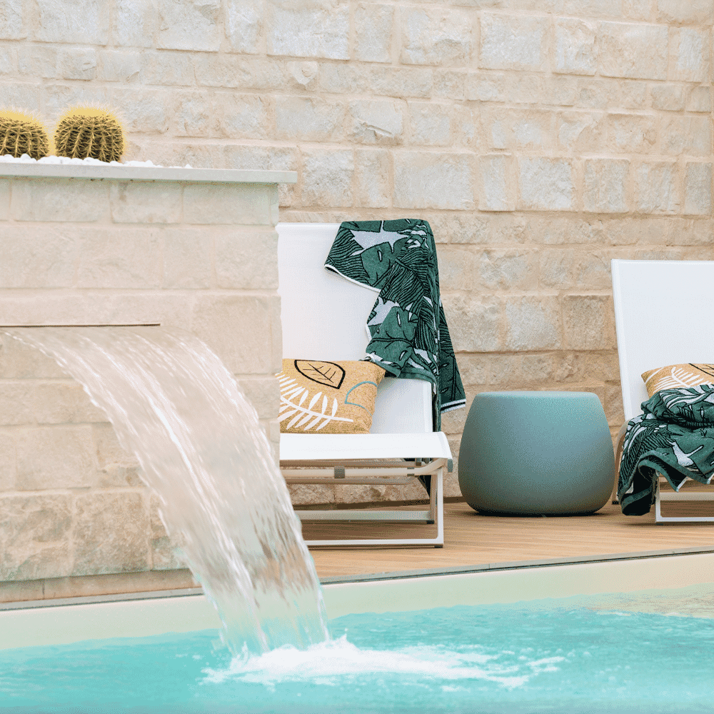 White lounge chairs by a pool featuring leaf-print towels and textured pillows.