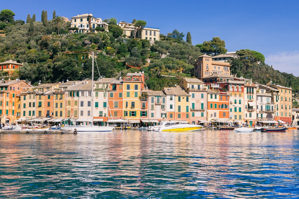 Peaceful waterfront with pastel houses and docked boats in a quiet Mediterranean harbor.