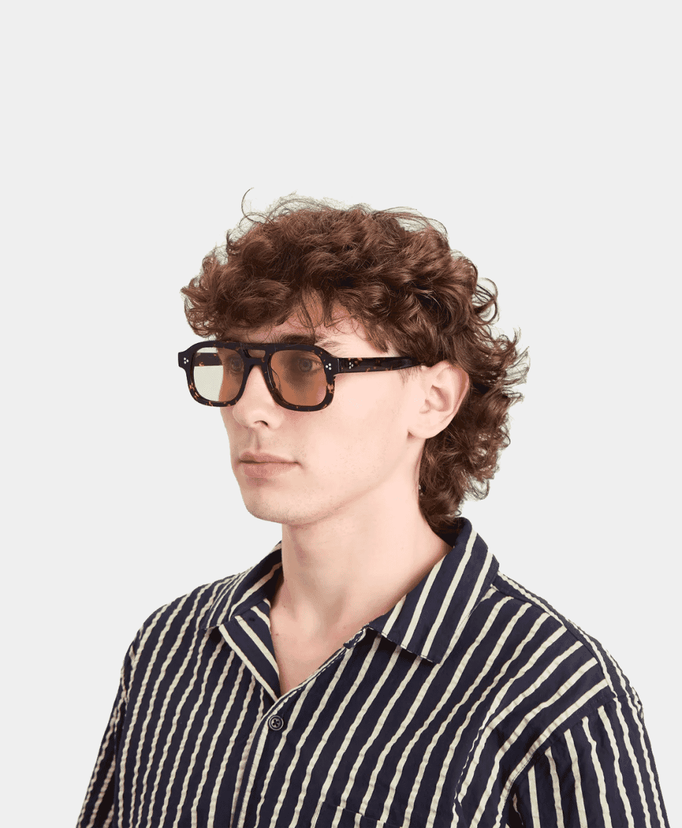 A man wearing tortoiseshell sunglasses and a striped shirt looking confident.