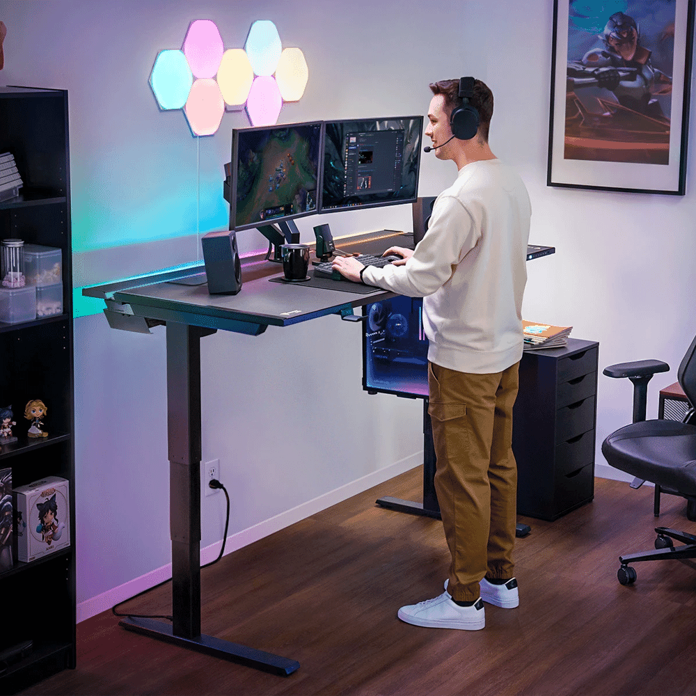 Man in a cream sweatshirt at a standing gaming desk with headphones and ambient lighting.