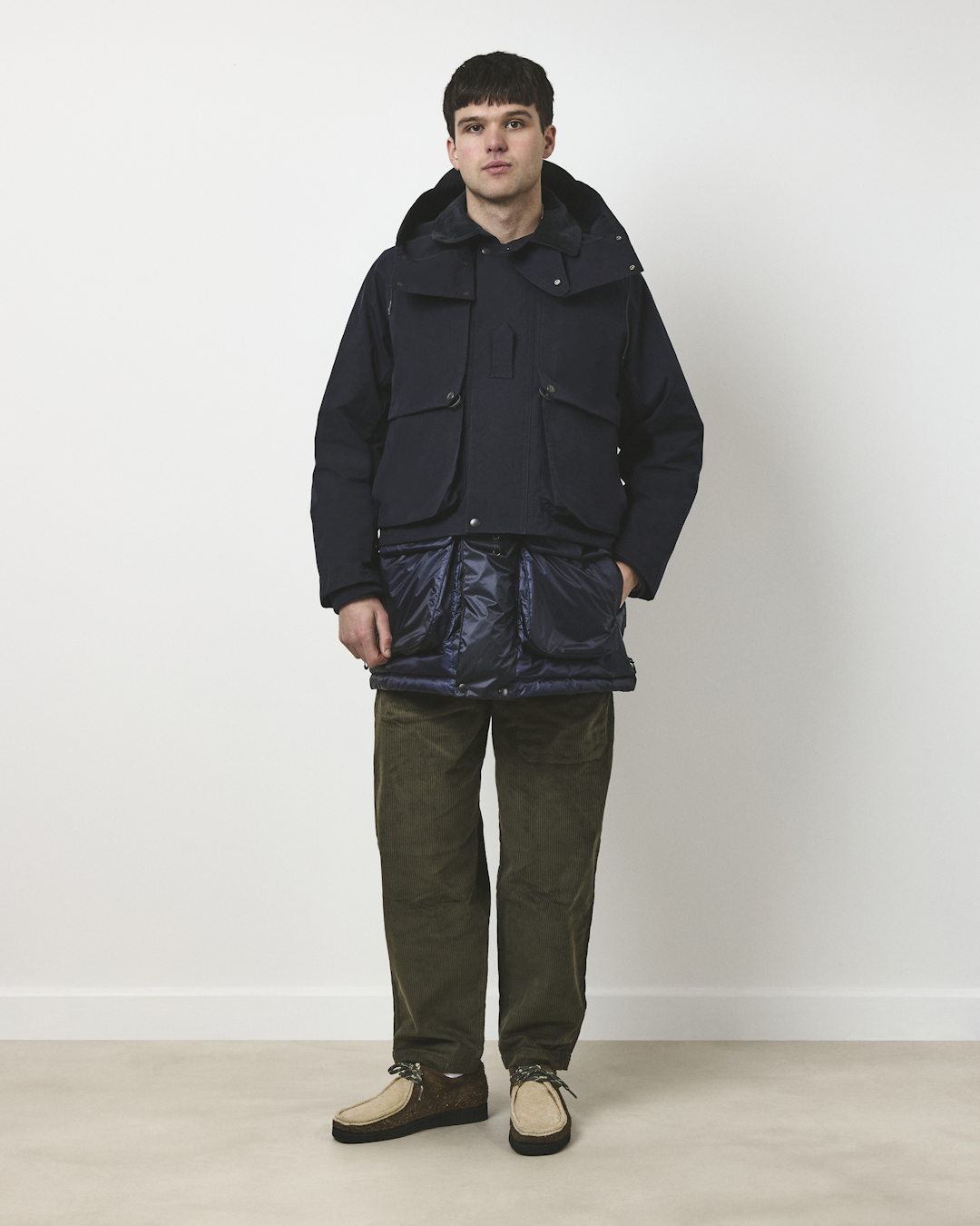 Man in a full navy parka outfit with olive corduroy trousers and suede footwear.