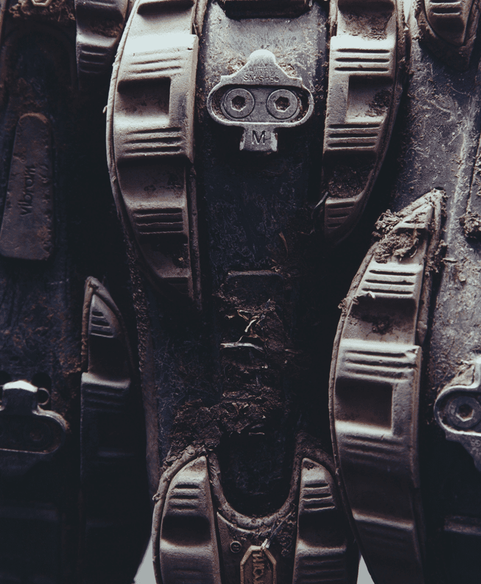 Close-up of a mud-covered cycling shoe with a metal cleat showing signs of heavy outdoor use.