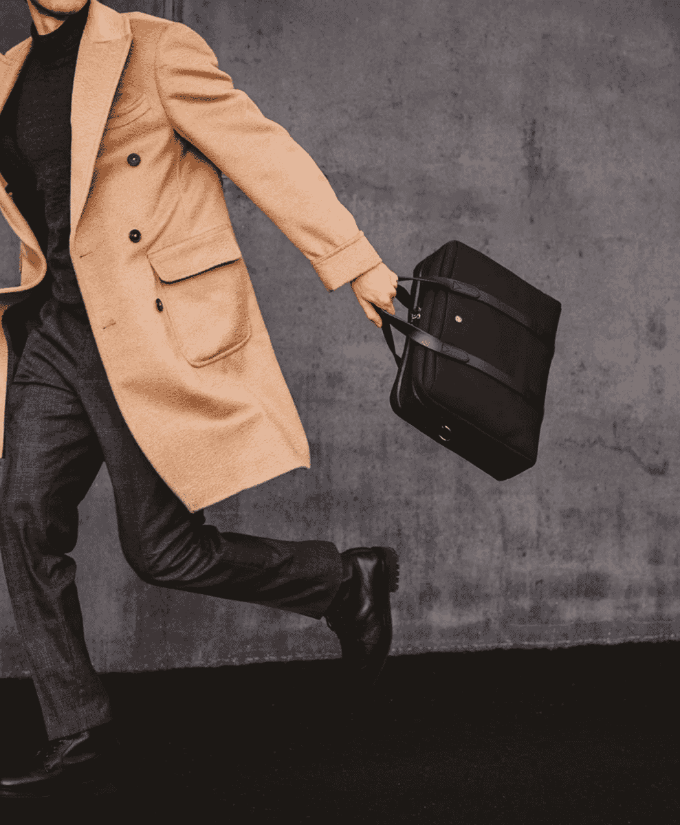 A man in a beige double-breasted wool coat and black turtleneck walking in a city.