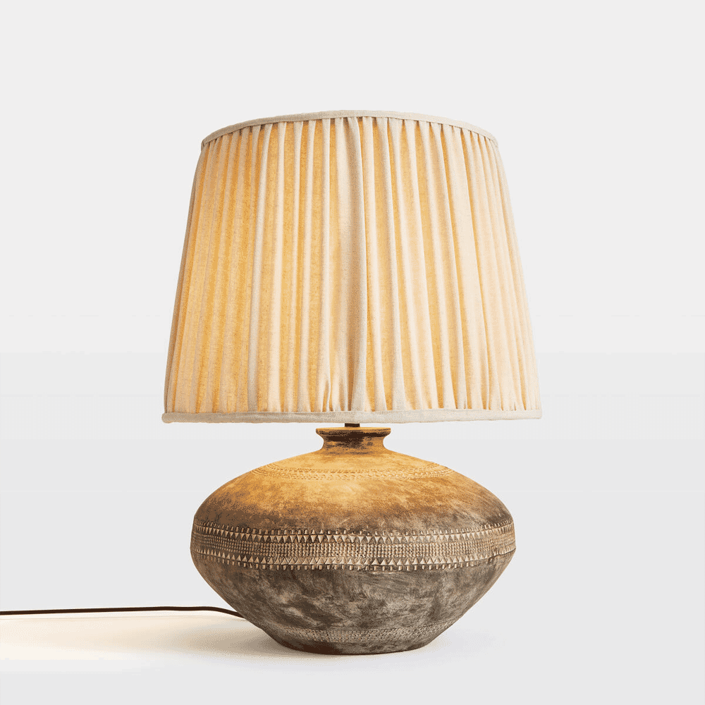 Artisanal ceramic table lamp with a pleated beige fabric shade and textured base.