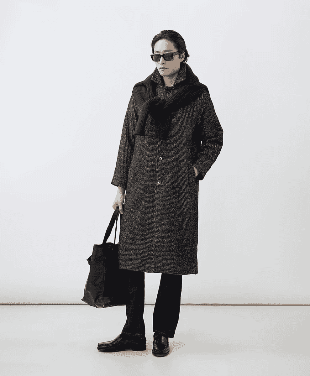 A man in a dark coat, chunky scarf, sunglasses, and carrying a tote bag.