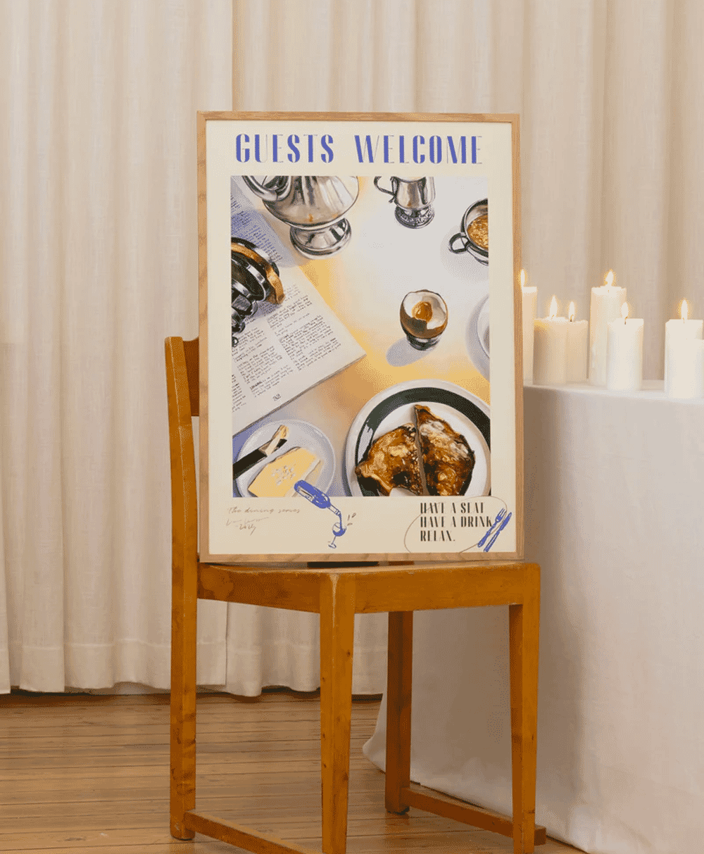 A 'GUESTS WELCOME' vintage poster on a chair next to lit candles, creating a welcoming atmosphere.
