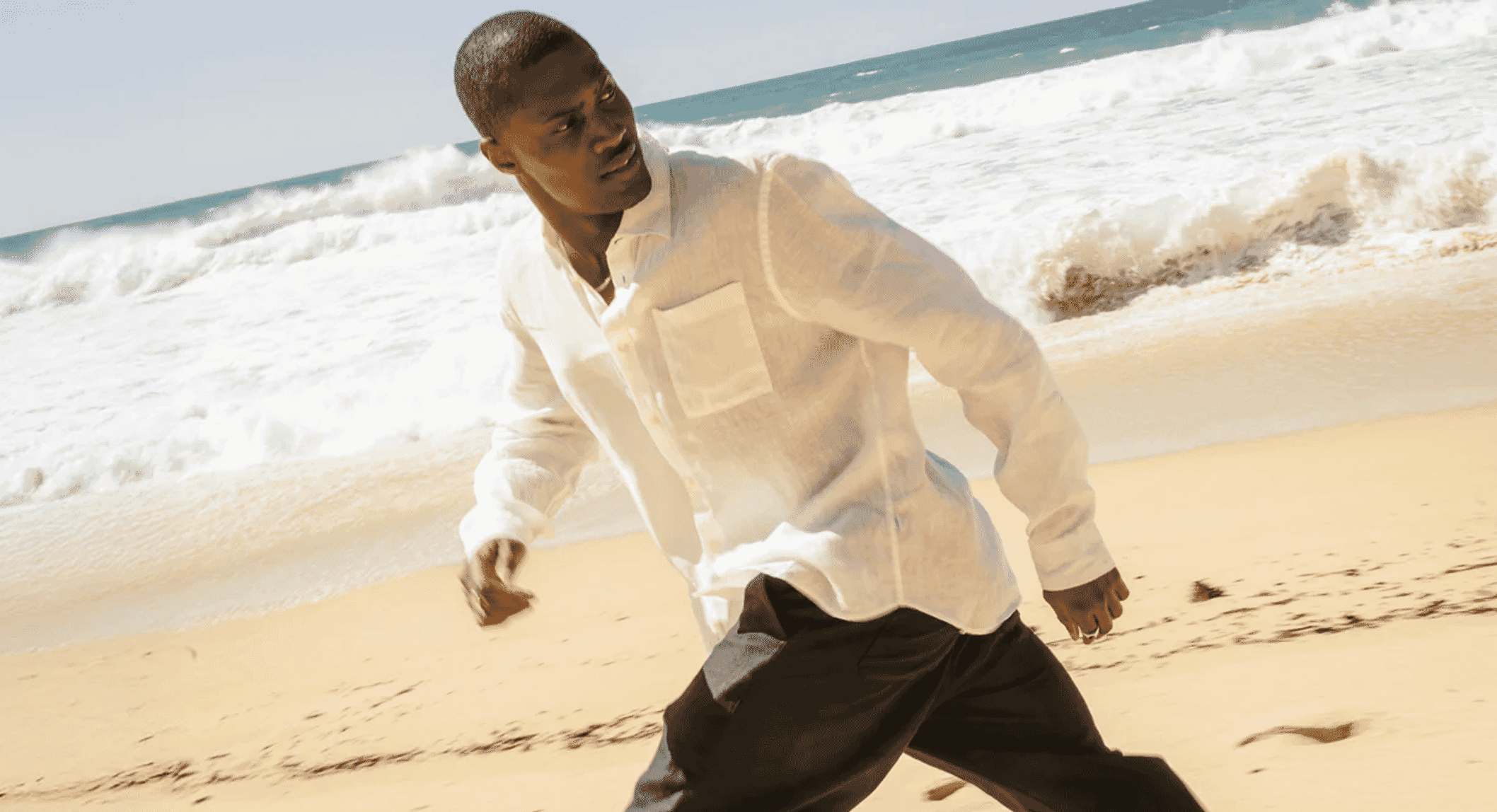 Man wearing white linen shirt running on a beach, conveying movement and lightness.