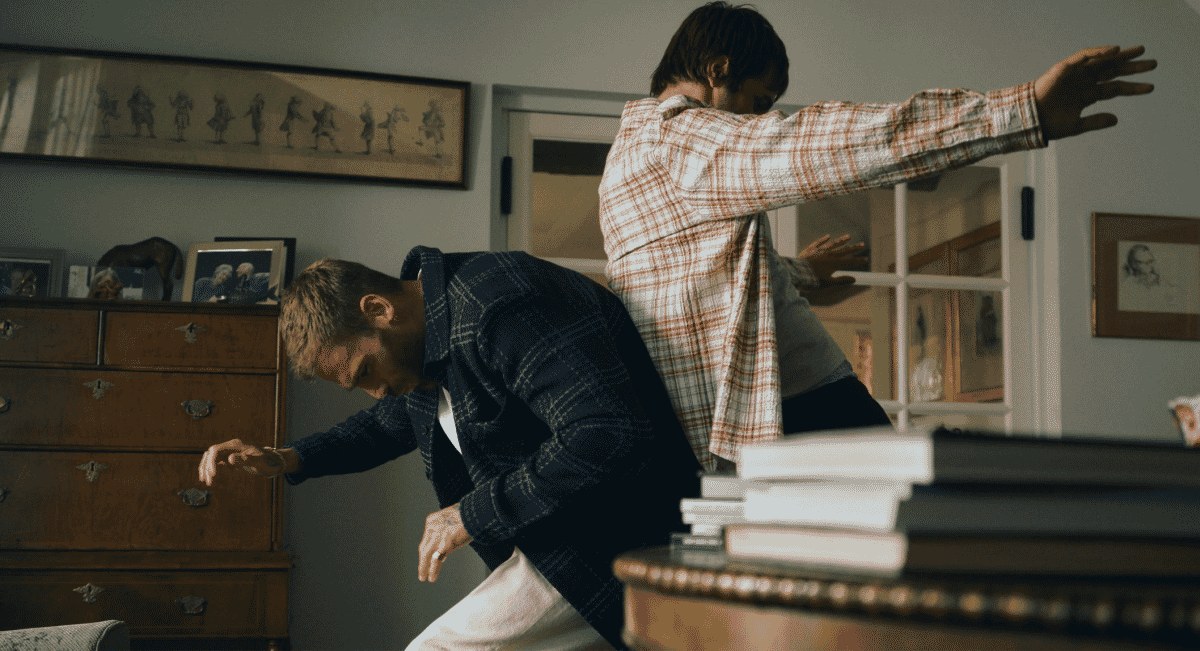 Two men in plaid shirts and jackets engaging in a physical struggle in a vintage-style room.