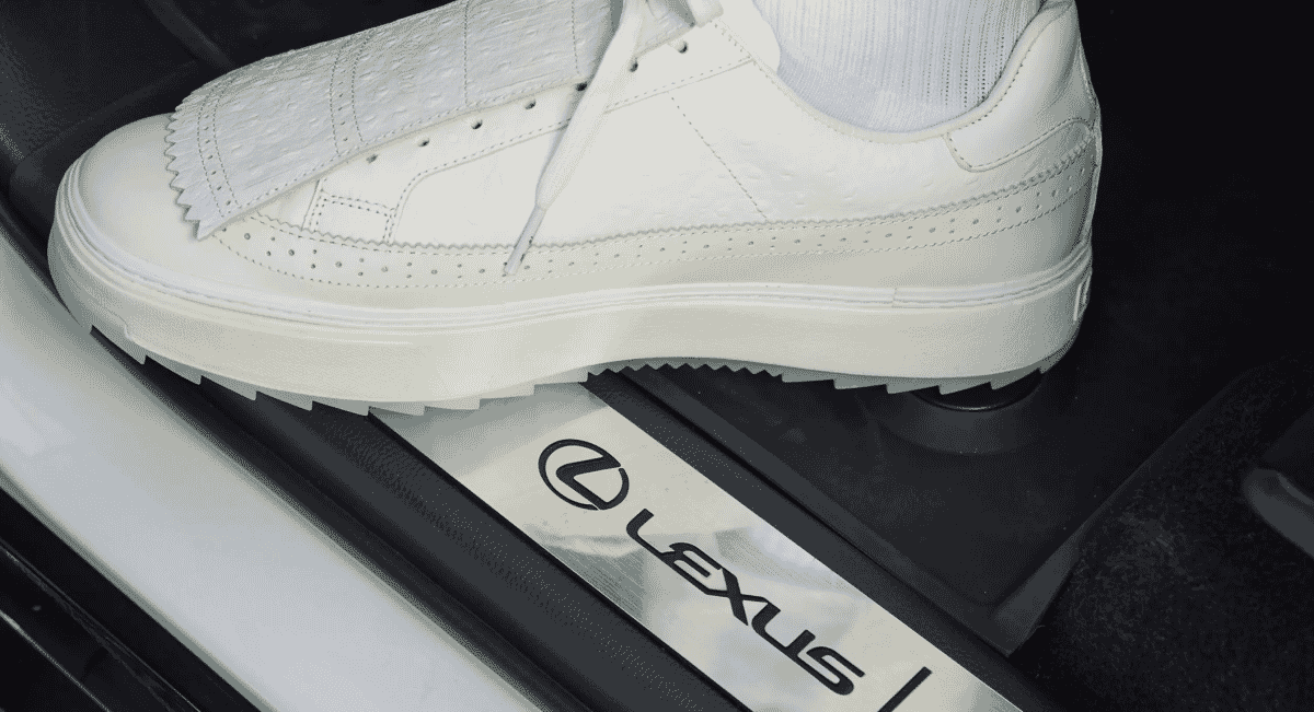 Detailed shot of a white brogue sneaker resting on the Lexus branded door sill.
