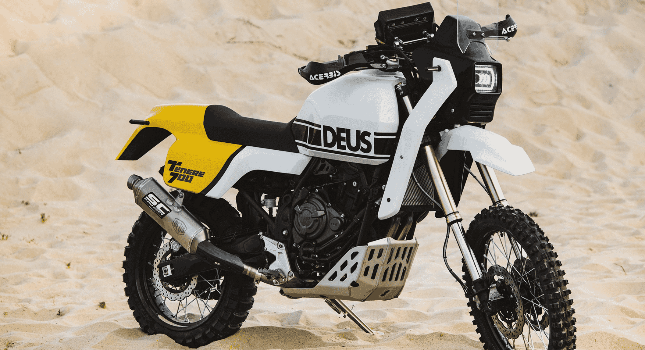 Wide profile shot of the custom Deus Yamaha Tenere 700 on sandy terrain with distinct branding.