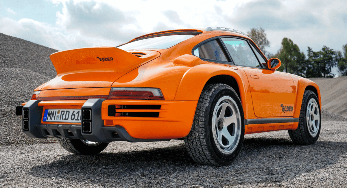An orange Porsche Rodeo modified for off-road use with high ground clearance and rugged tires on gravel.