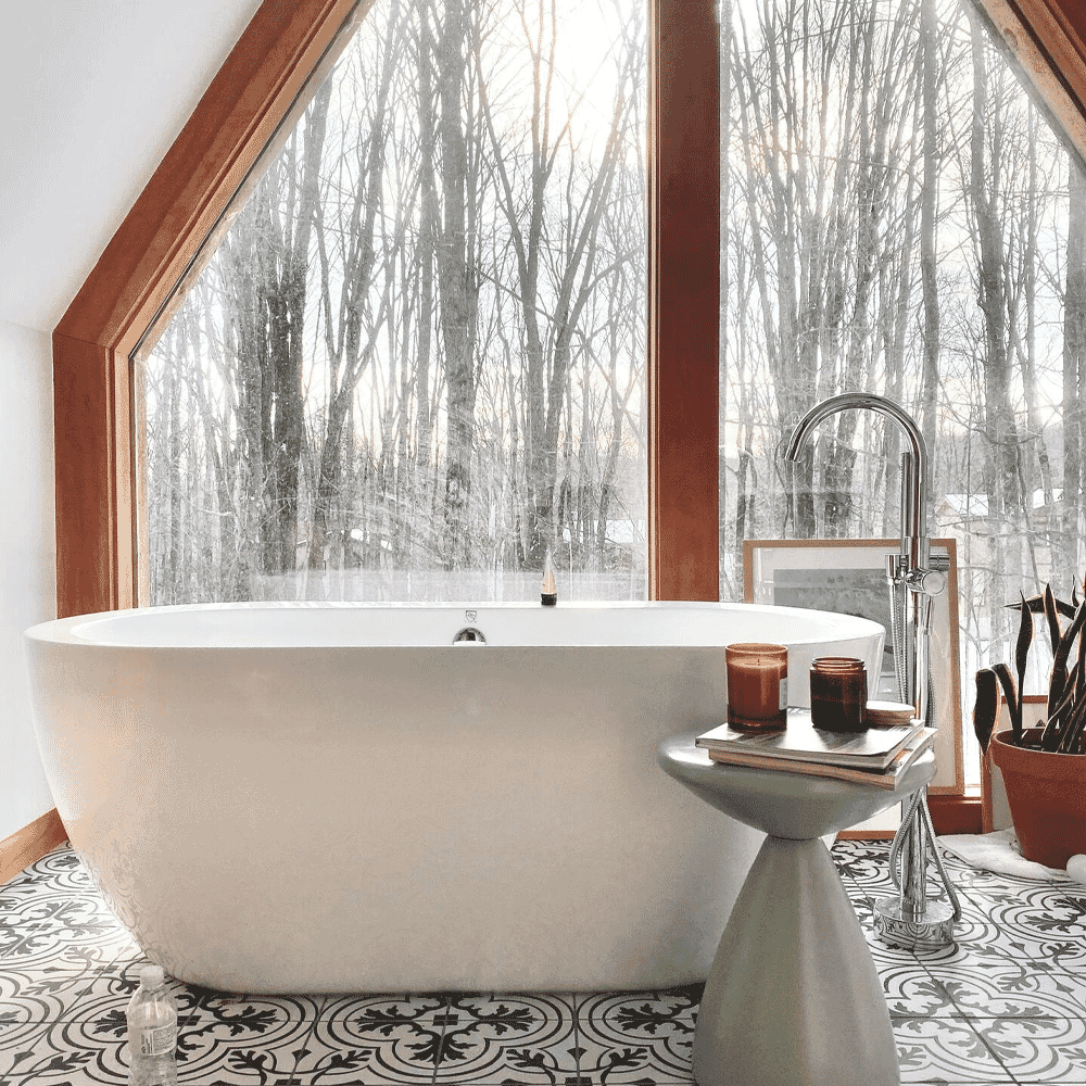 Freestanding bathtub under a triangular window overlooking a snowy forest.