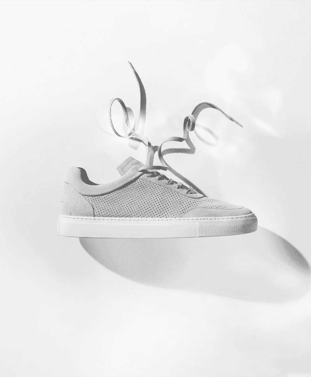 A modern white perforated sneaker with untied laces floating against a gradient background.