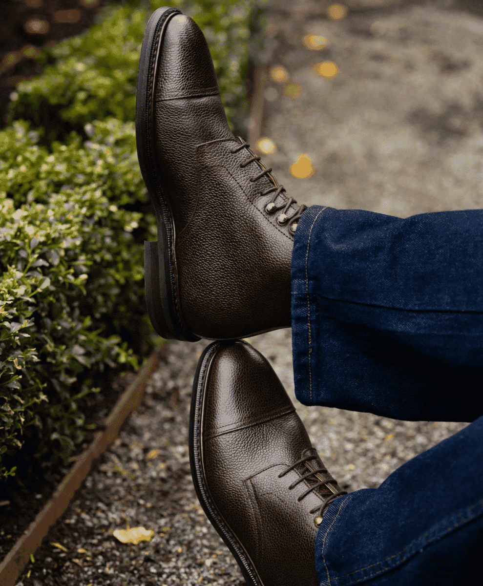 Close-up of dark brown pebbled leather cap-toe boots on gravel.