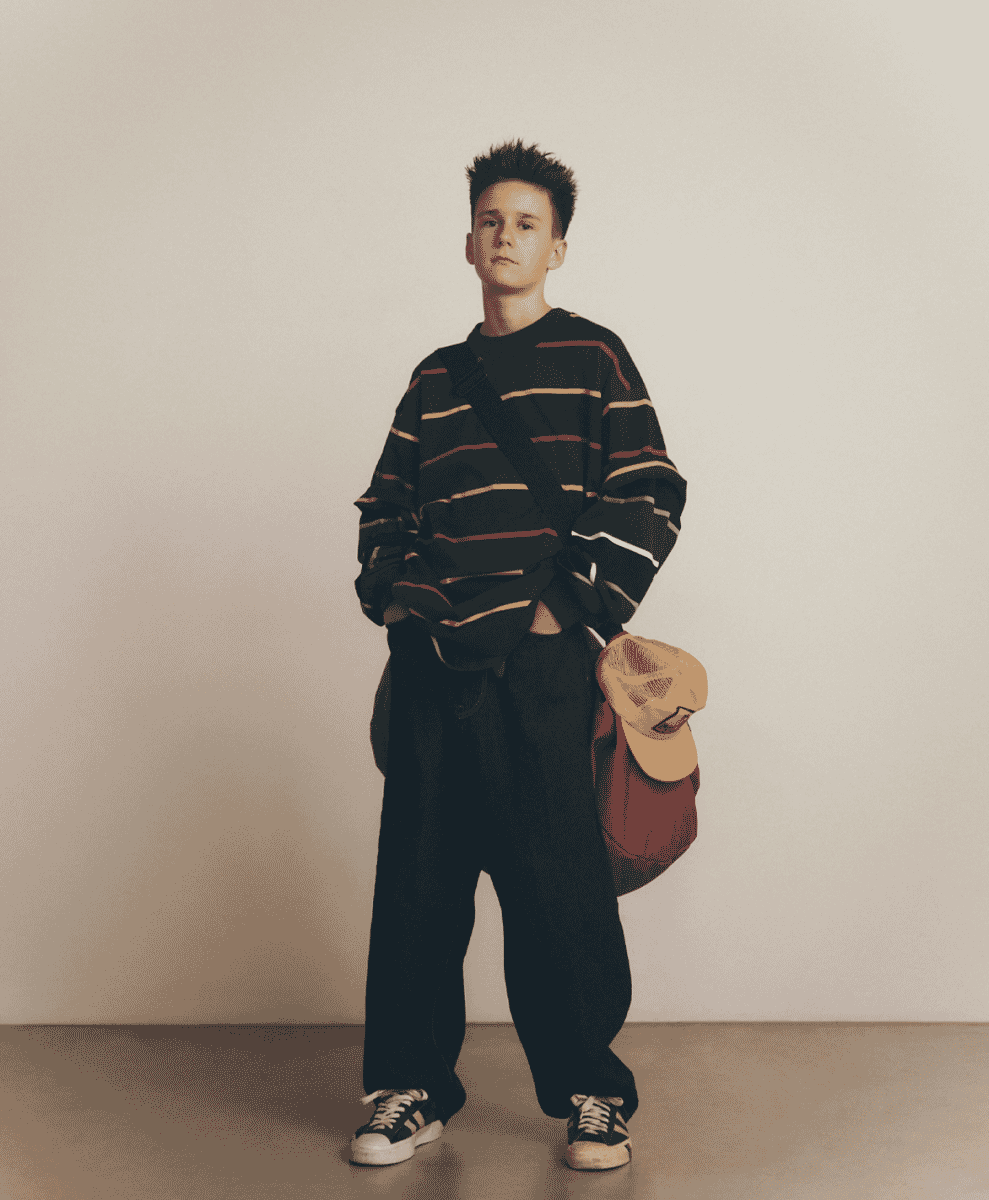 Model in an oversized striped sweater and baggy black trousers with a shoulder bag.