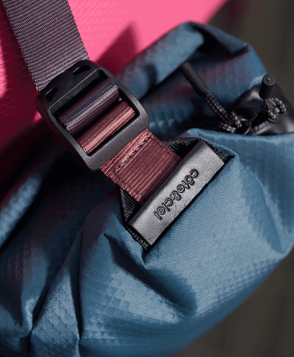 Close-up of a blue textured backpack with a red adjustable strap and branded metal plate.